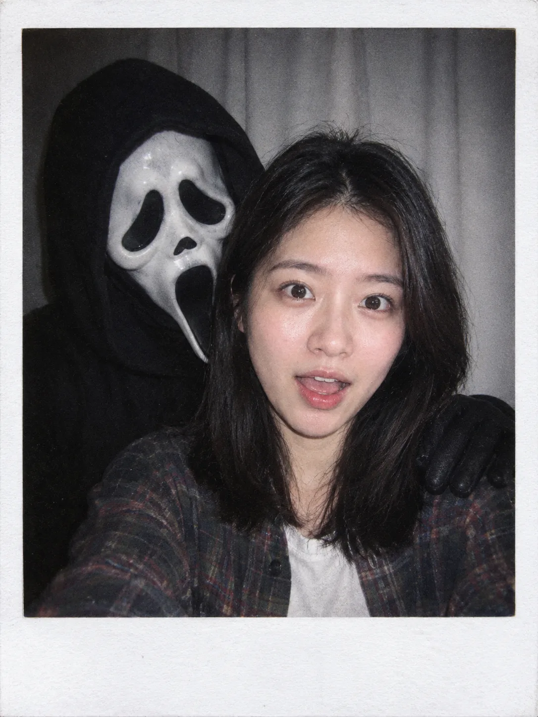 Polaroid of a woman in a plaid shirt, mouth open in surprise, while Ghostface rests a gloved hand on her shoulder